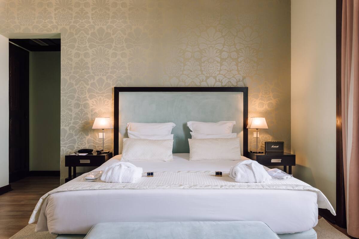 A neatly made bed with white linens, two bedside tables with lamps, and a patterned wallpaper.