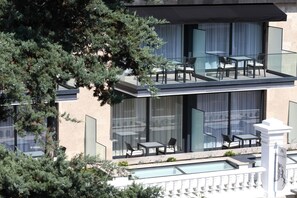 Un edificio moderno con balcón de vidrio, mobiliario exterior y piscina.