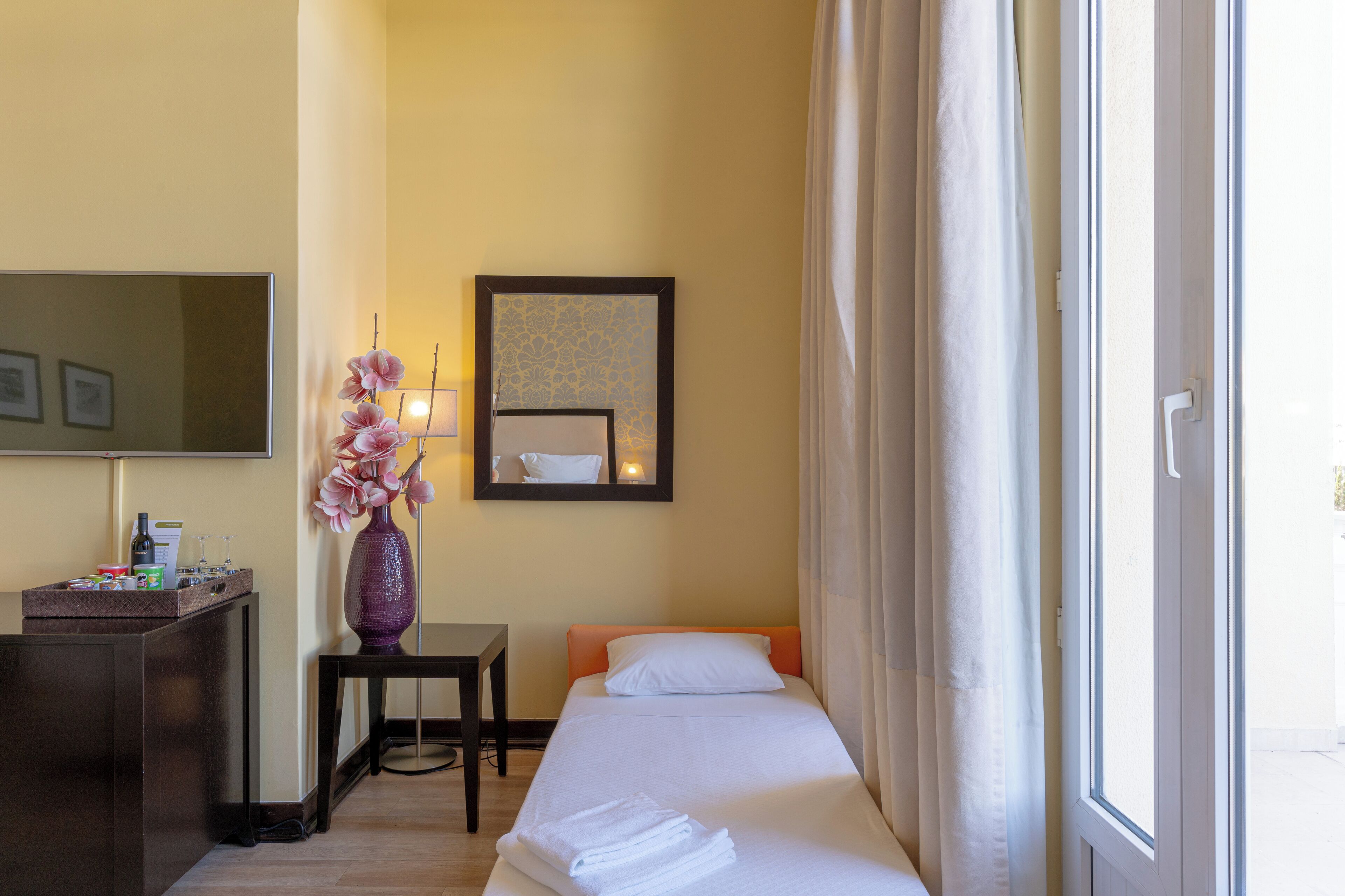 Una habitación de hotel con cama, escritorio, espejo y ventana con cortinas.