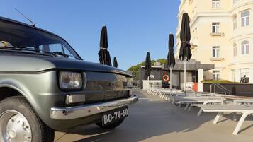 A vintage car parked in front of a building with outdoor seating and umbrellas.