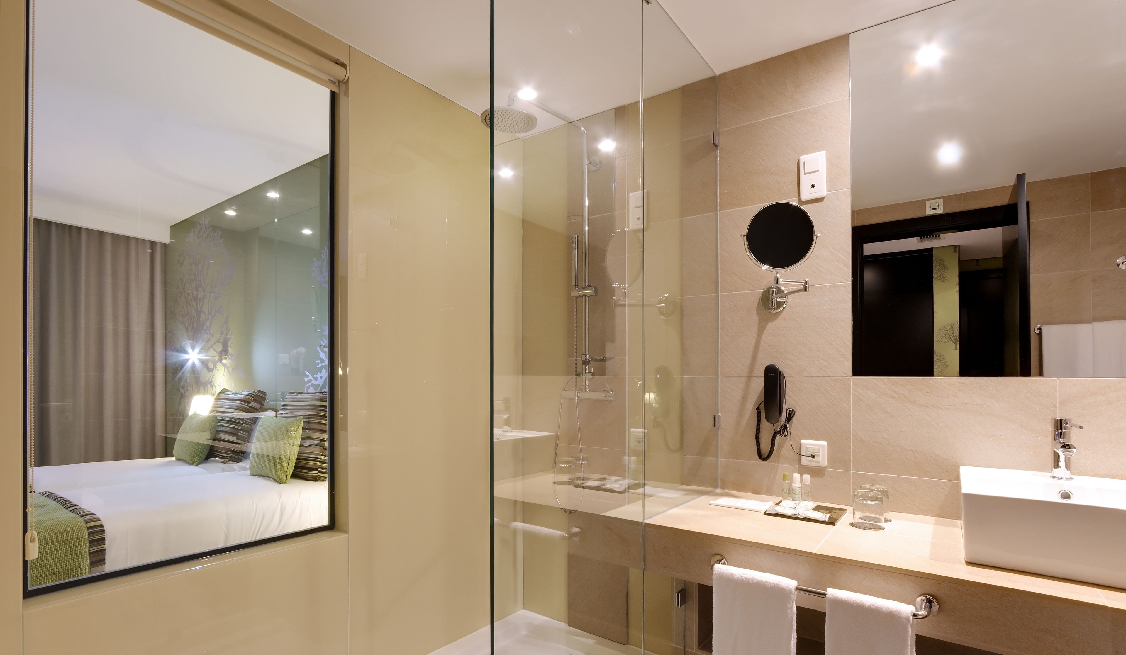 Une salle de bain d’hôtel moderne dotée d’une douche à parois de verre, d’un meuble-lavabo et d’un grand miroir.