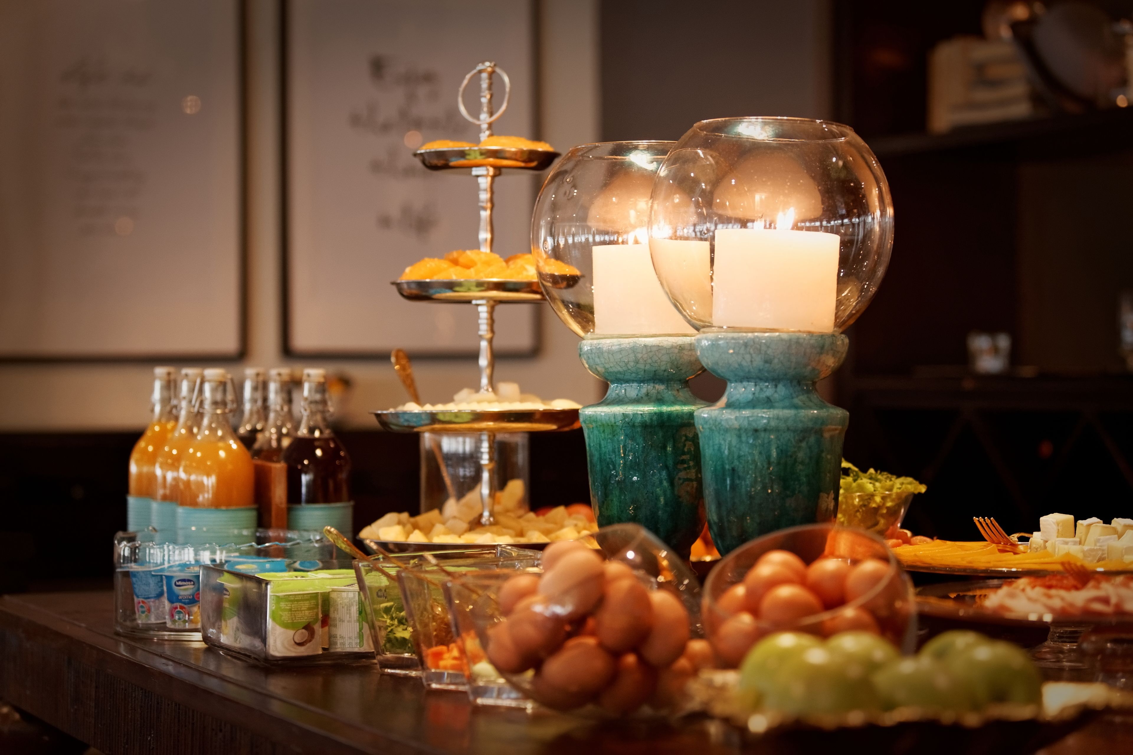 A buffet with various food items and beverages, including a three-tiered dessert stand and a candle centerpiece.