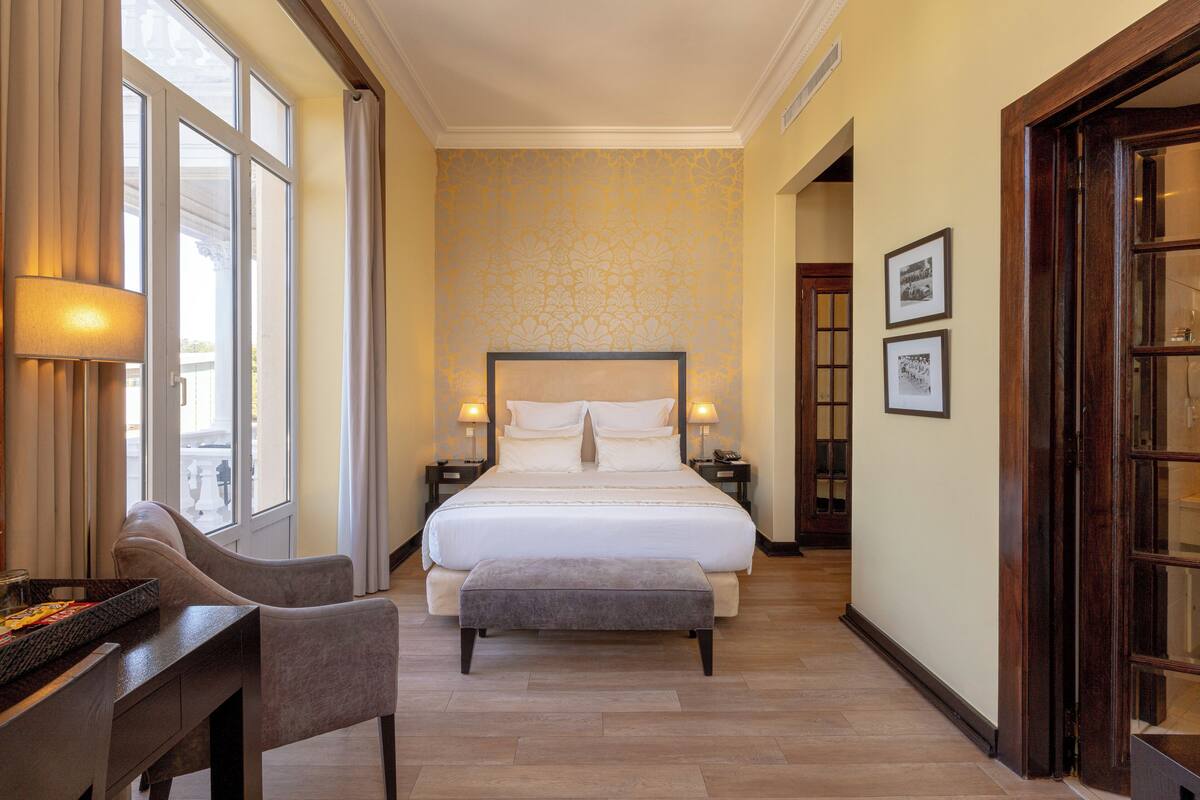 A hotel room with a large bed, a desk, and a chair. There are two bedside tables with lamps.