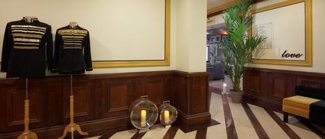 A lobby with a reception desk, two mannequins in formal attire, a potted plant, a wall with a 'love' sign, and a striped floor.