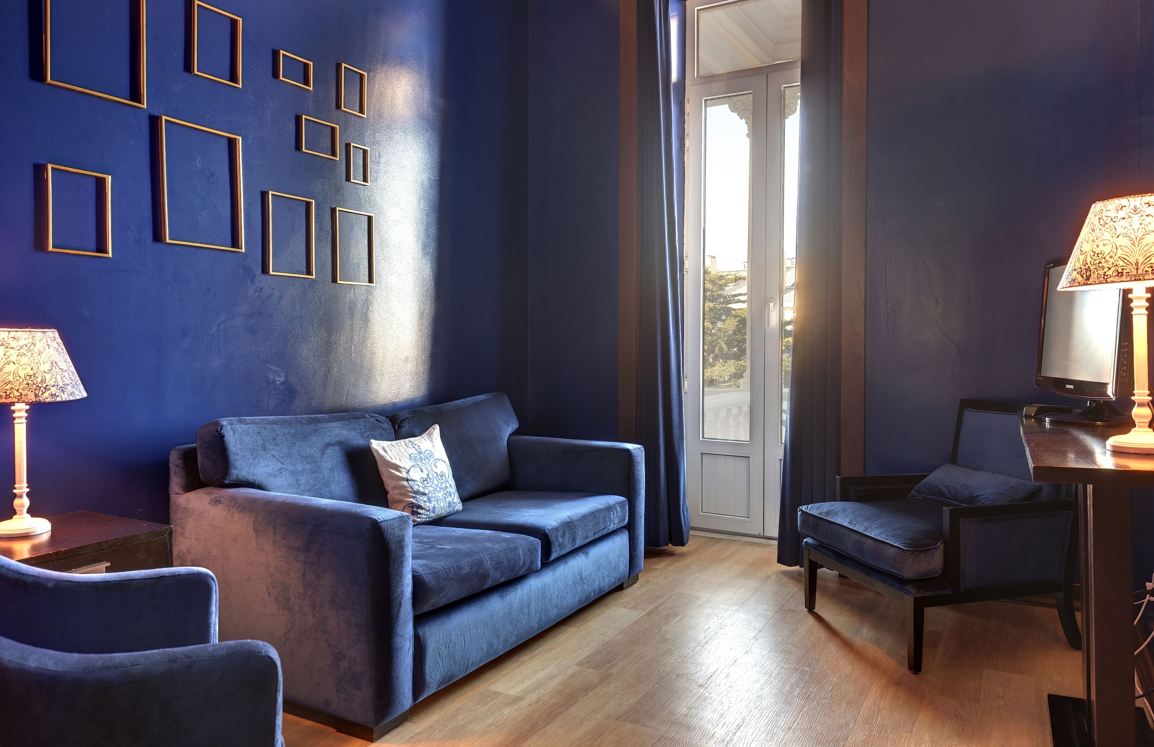 A room with a blue wall, a sofa, a chair, a lamp, and a view through a door.