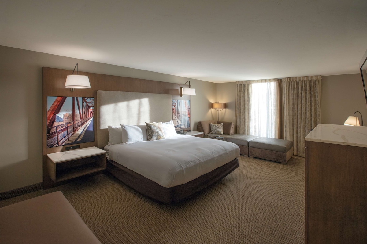 Une chambre d’hôtel avec un grand lit, un bureau, une chaise, un canapé, une télévision et une lampe.
