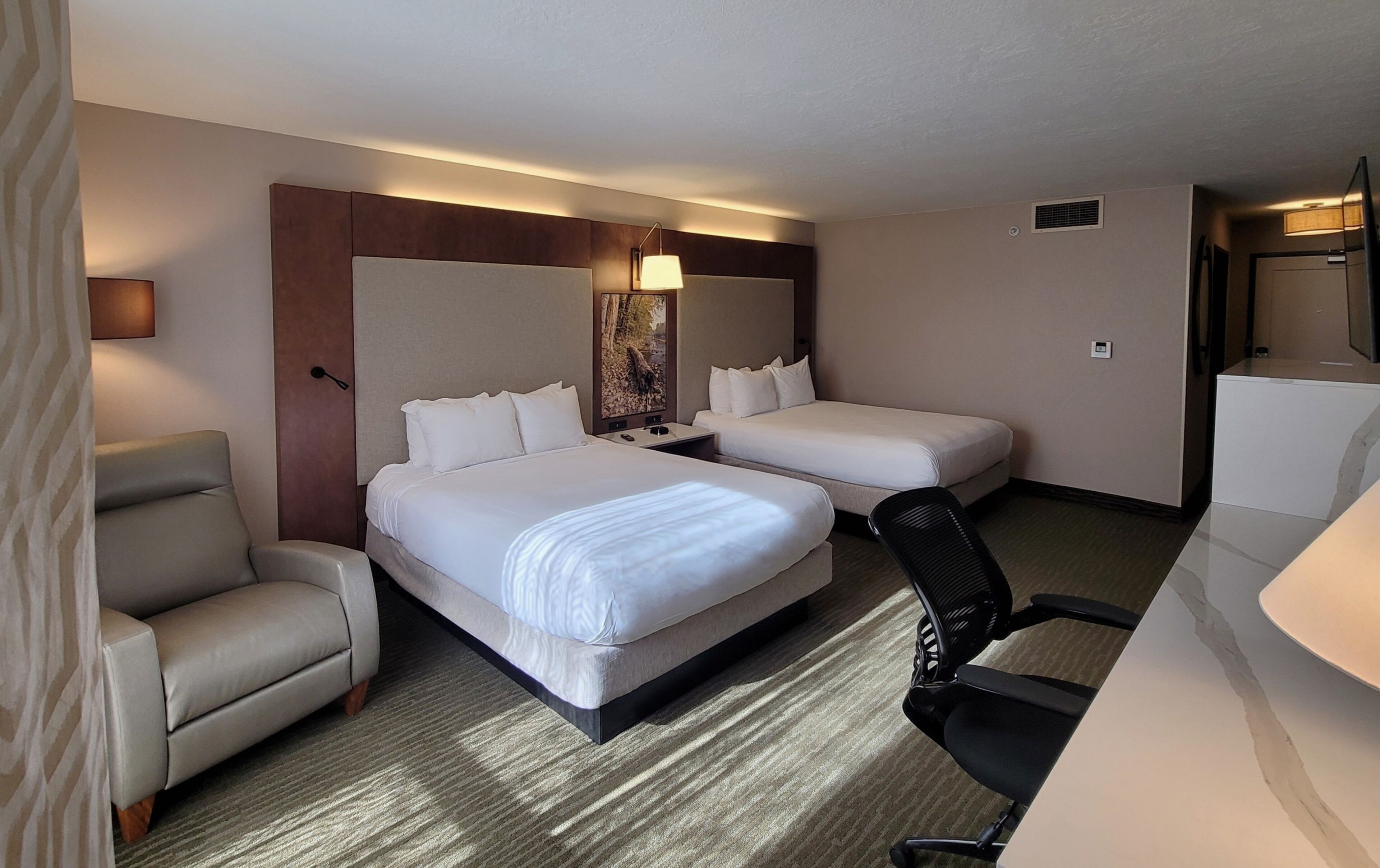Une chambre d’hôtel avec deux lits, un canapé, une chaise, un bureau et une lampe.
