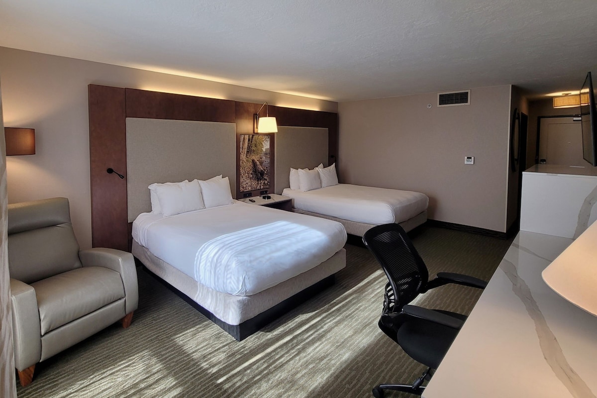 A hotel room with two beds, a sofa, a chair, a desk, and a lamp.