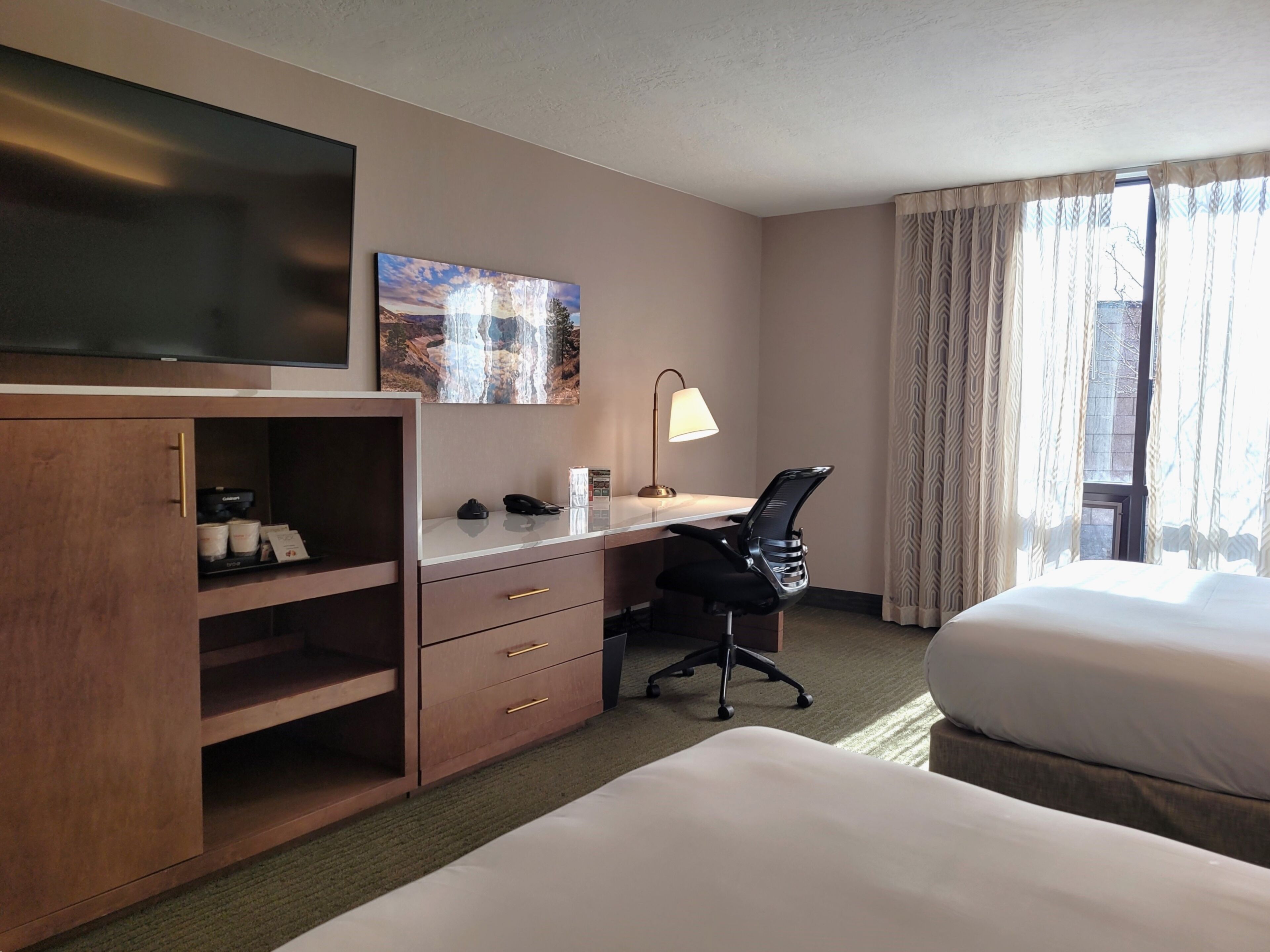 Een hotelkamer met een bed, een bureau met stoel, een televisie en een schilderij aan de muur.