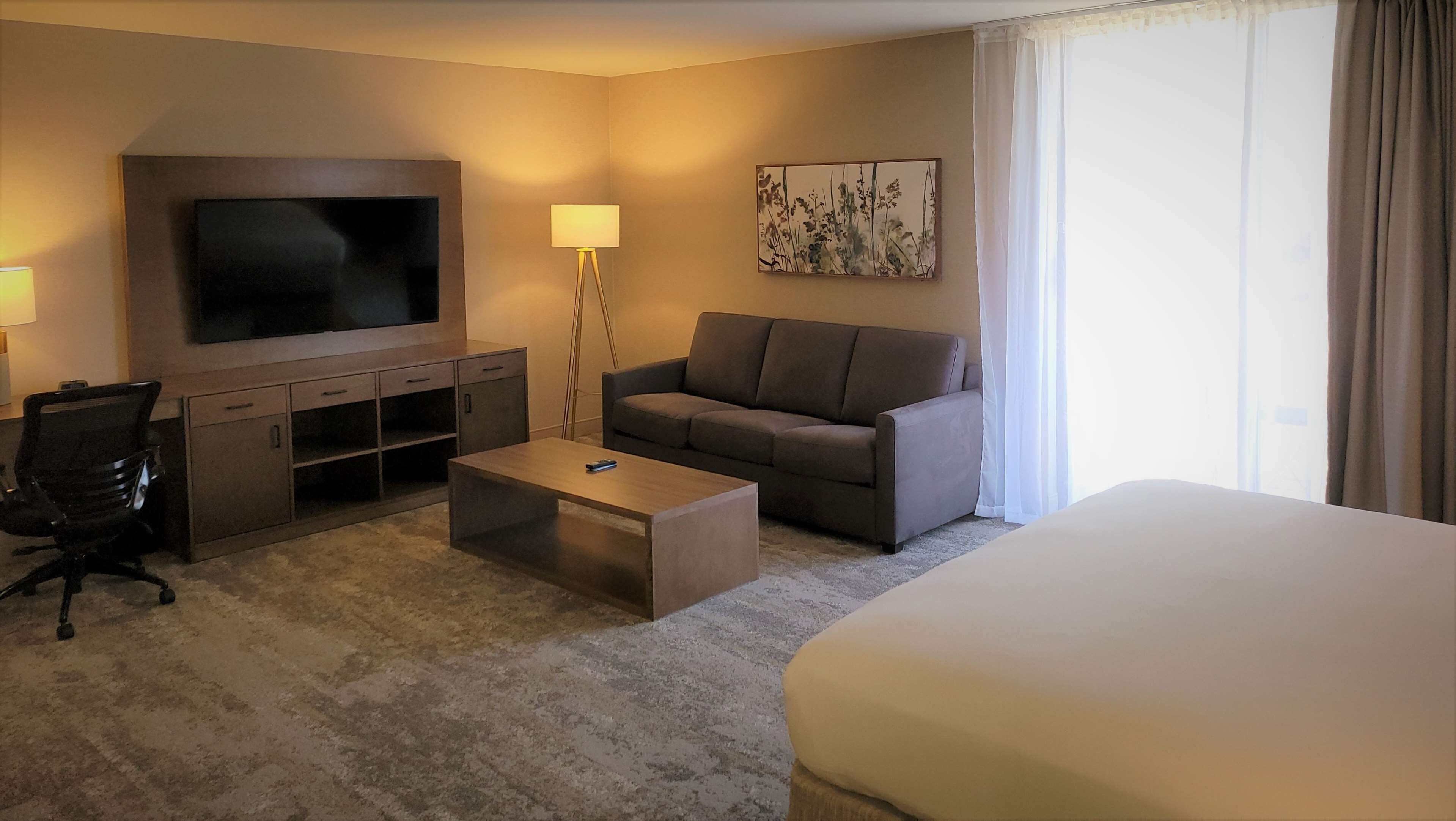 A hotel room with a TV, sofa, coffee table, and a bed.