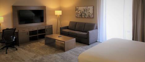 A hotel room with a TV, sofa, coffee table, and a bed.