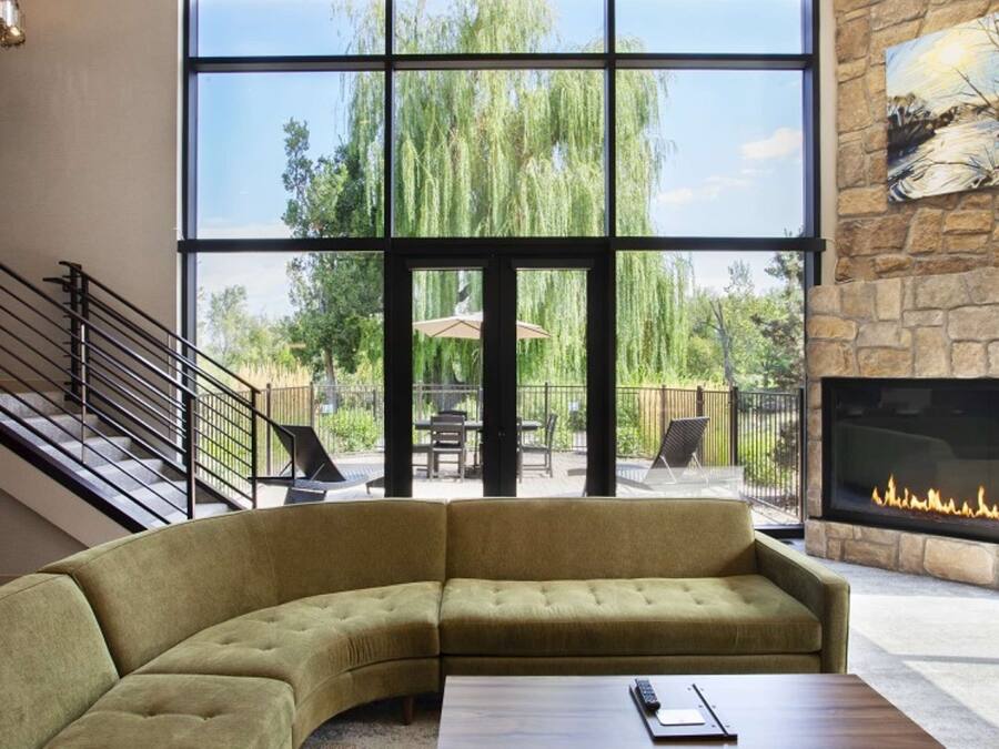 A modern living room with a curved sofa, a fireplace, a staircase, and large windows overlooking a garden.