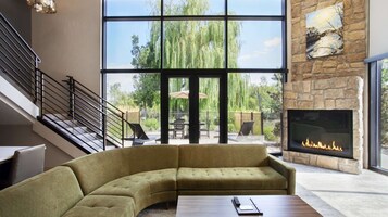 Un salón moderno con un sofá curvo, una chimenea, una escalera y ventanas amplias que dan a un jardín.
