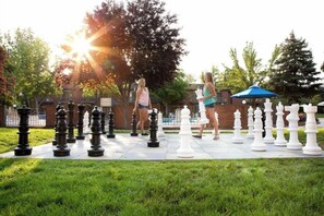 A chessboard set outdoors with two people standing on it.