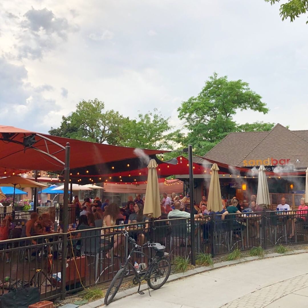 Ein Außenbereich zum Essen mit Tischen und Stühlen, der von roten Sonnenschirmen beschattet wird, und ein Fahrrad in der Nähe.