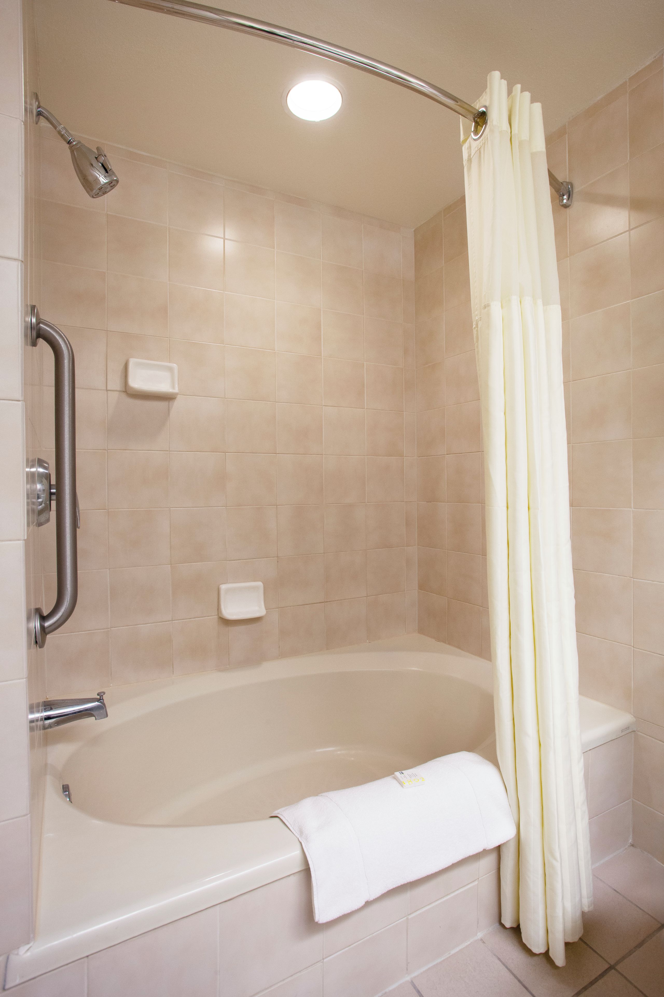 A bathroom with a bathtub, a shower, and a handrail.