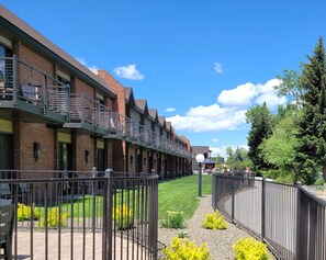 A row of brick buildings with a green roof, a metal fence, and a grassy area with yellow flowers. - The Riverside Hotel, BW Premier Collection (Boise)