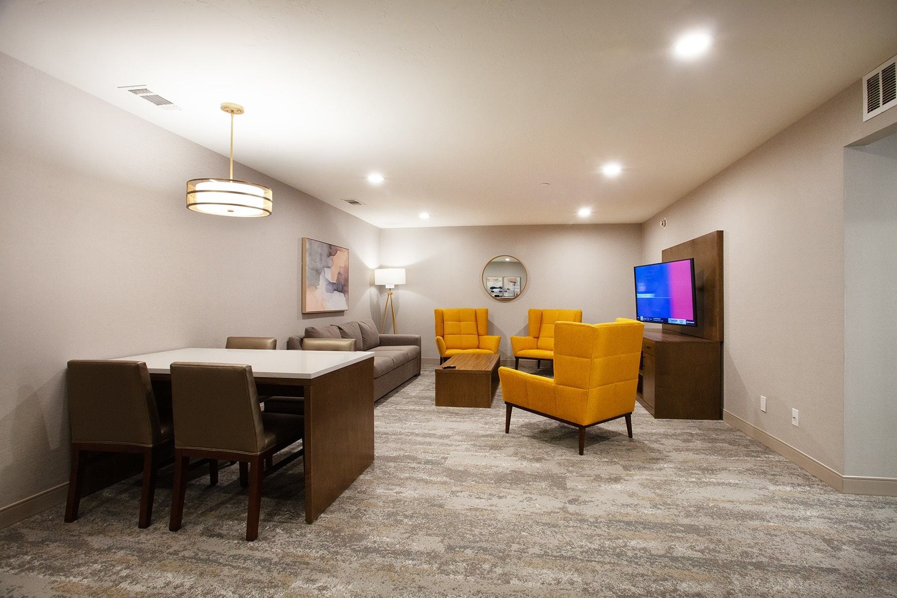A room with a dining table, chairs, a sofa, a TV, and a lamp.