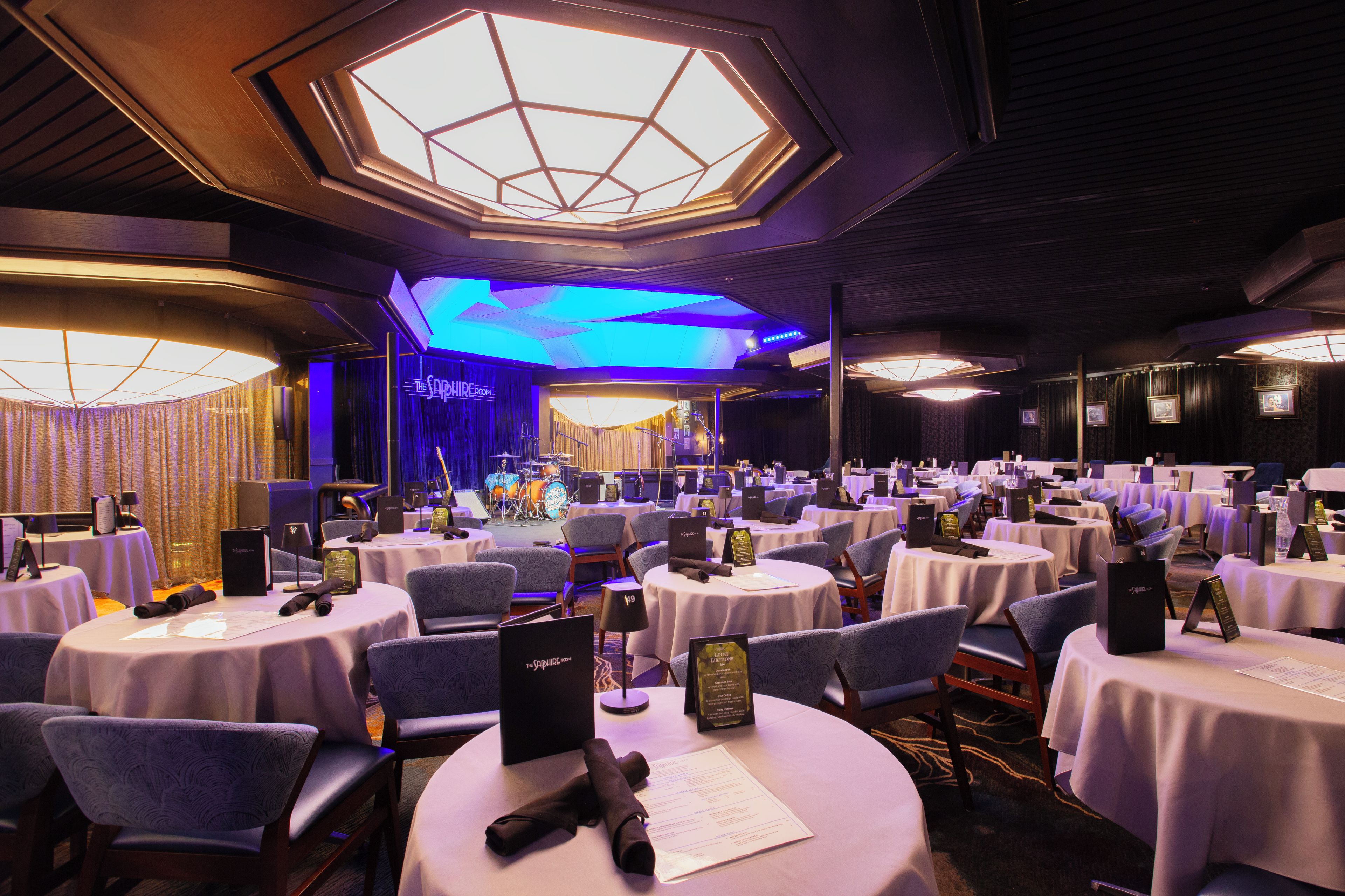 A banquet hall with round tables, chairs, and a stage area.