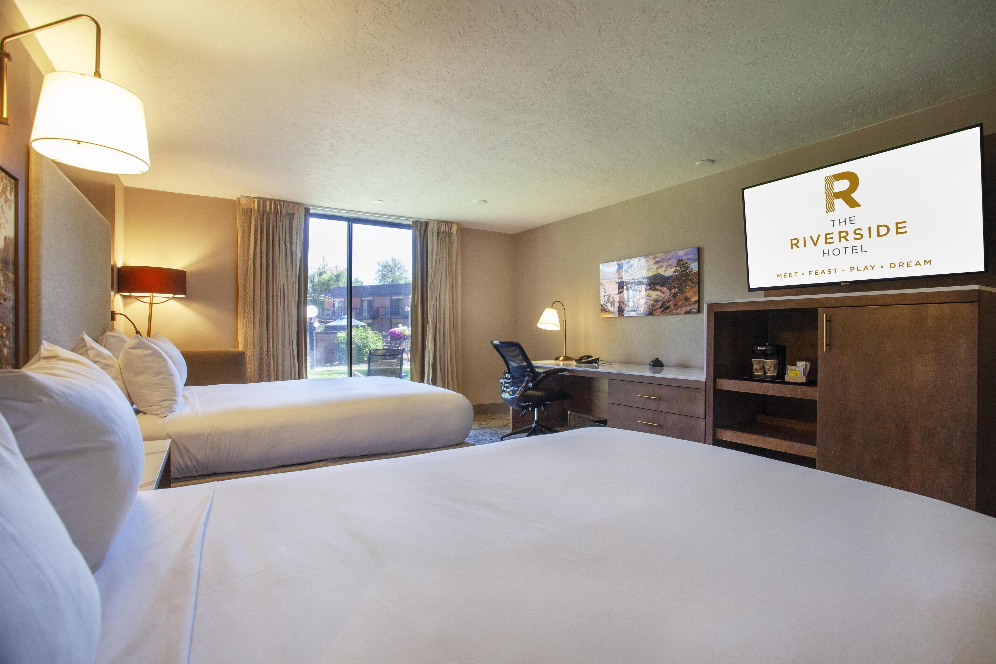 A hotel room with two beds, a desk, a chair, a TV, and a window with curtains.
