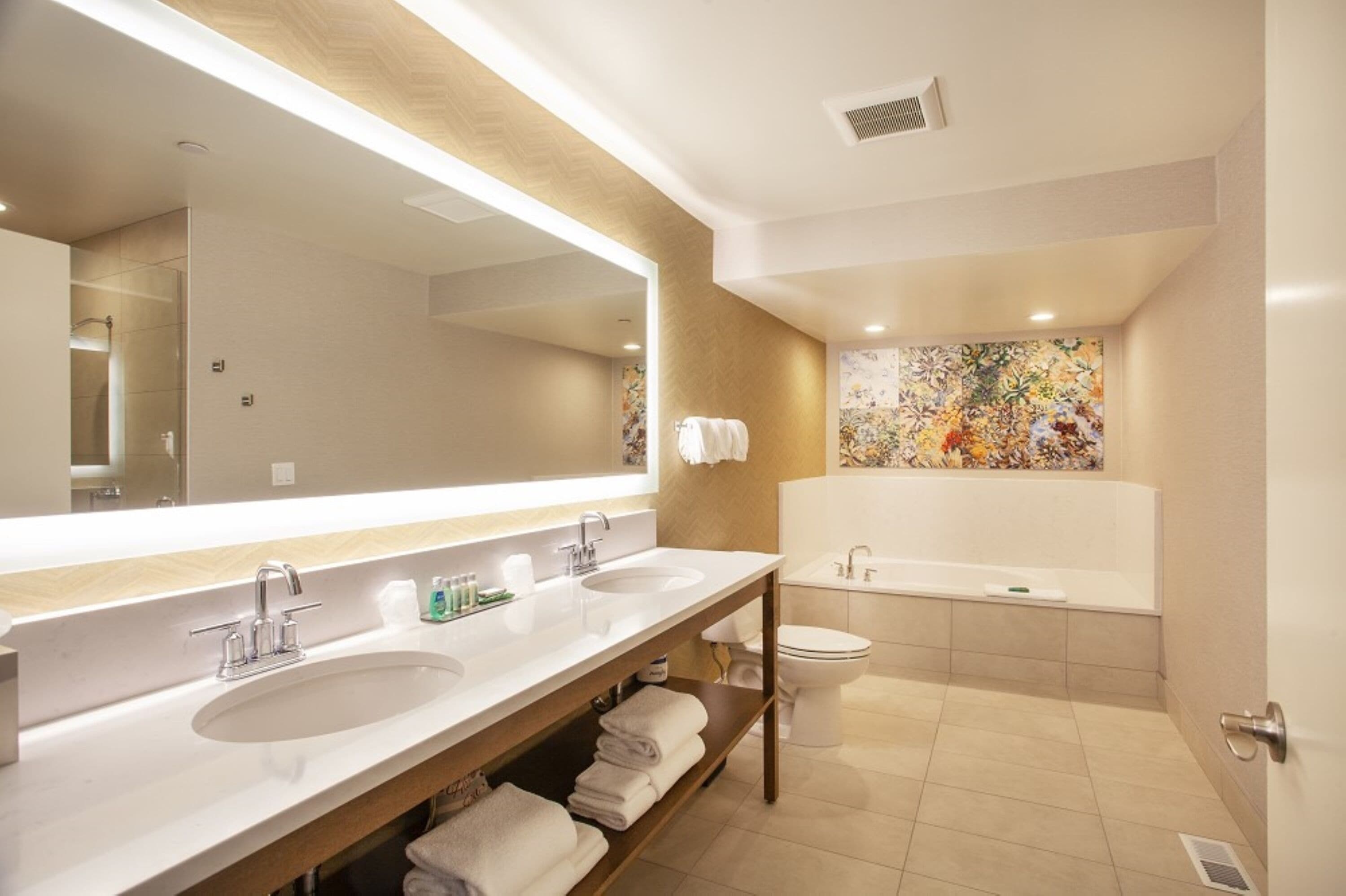 A modern bathroom with two sinks, a large mirror, a bathtub, and a toilet.