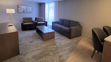A modern living room with a sofa, two armchairs, a coffee table, and a desk with a lamp.
