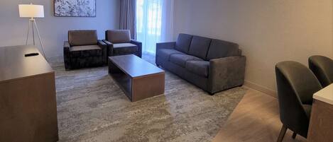A modern living room with a sofa, two armchairs, a coffee table, and a desk with a lamp.