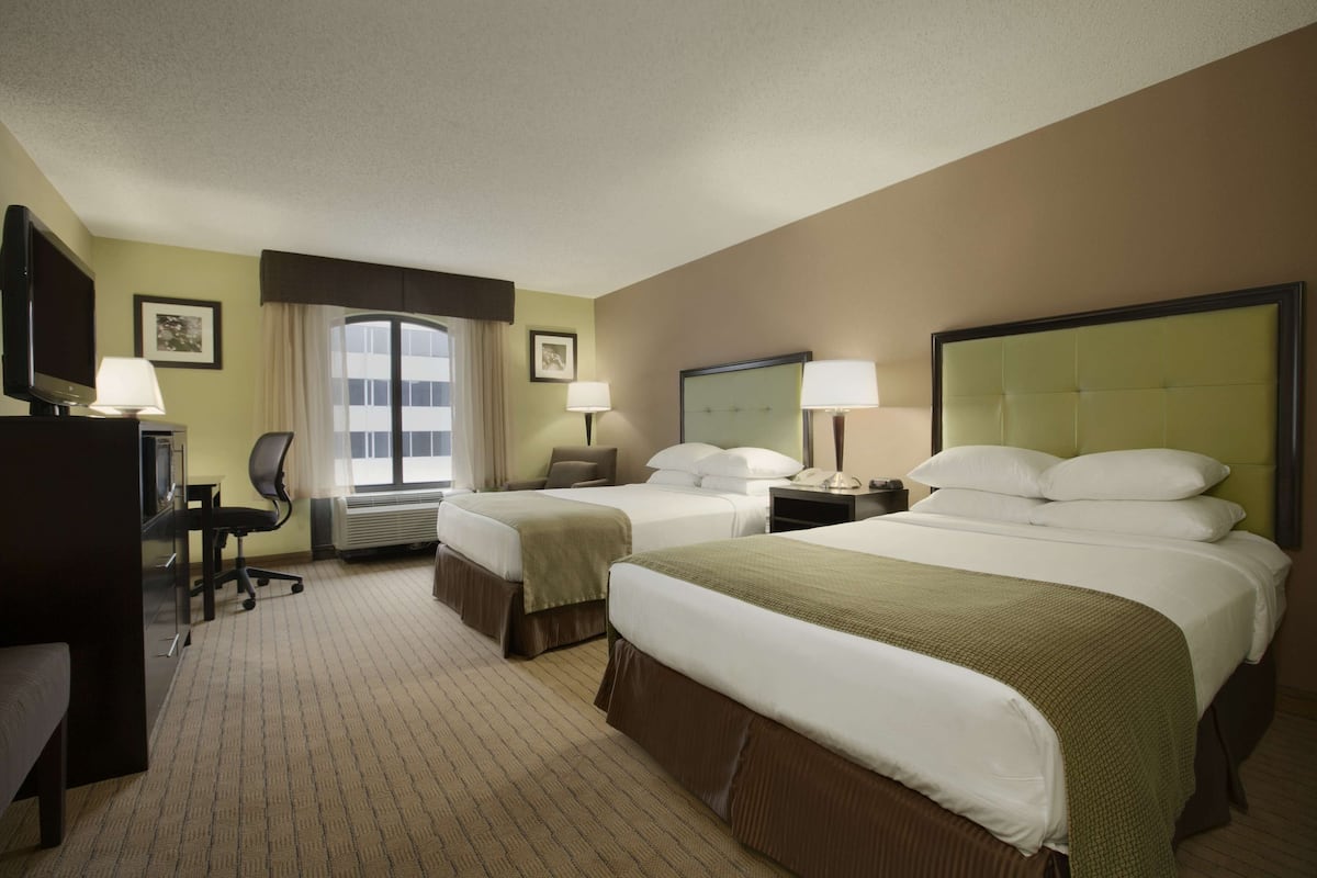 A hotel room with two beds, a desk, a chair, and a television.