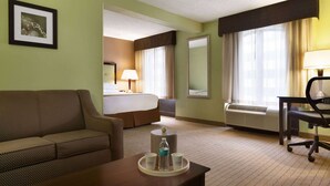 Ein Hotelzimmer mit Bett, Sofa, Schreibtisch und Stuhl. Auf einem Tablett befinden sich eine Flasche und zwei Tassen.