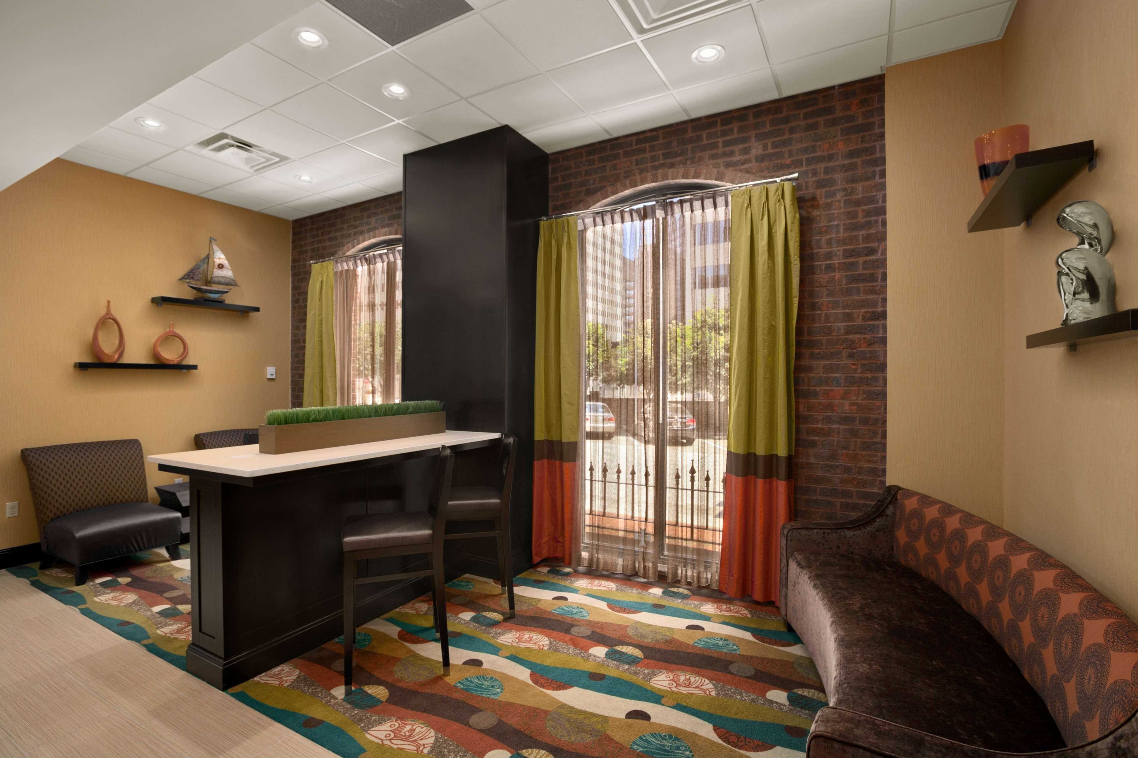 A hotel room with a bar area, a sofa, a patterned carpet, and a brick wall.
