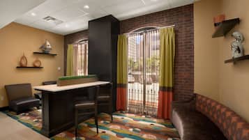 A hotel room with a bar area, a sofa, a patterned carpet, and a brick wall.