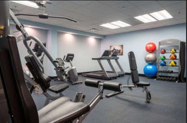 A gym with exercise equipment, a treadmill, and a set of exercise balls.