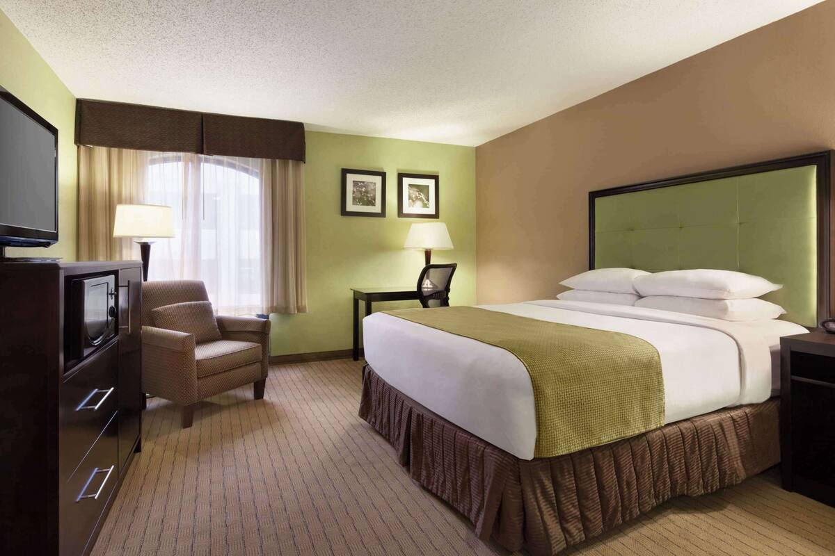 A hotel room with a bed, a chair, a desk, a television, and two framed pictures on the wall.
