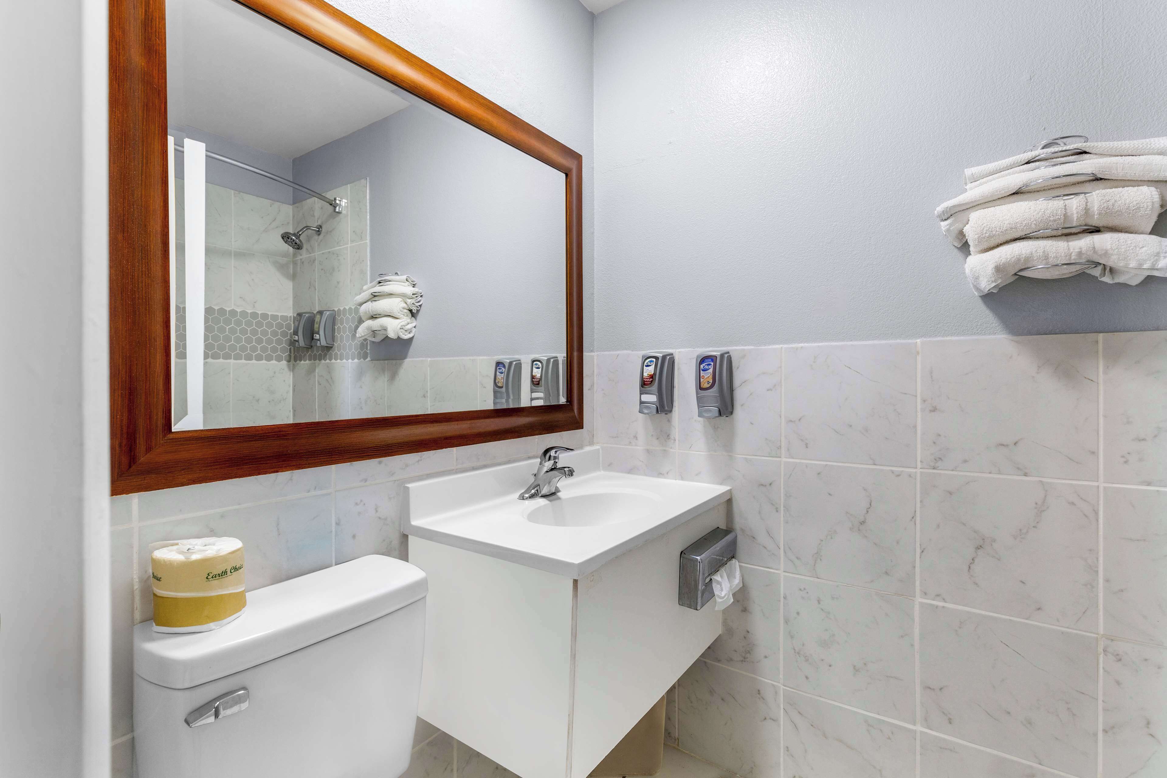 Un baño con un lavamanos blanco, un inodoro, un espejo con marco de madera y un perchero con toallas dobladas.