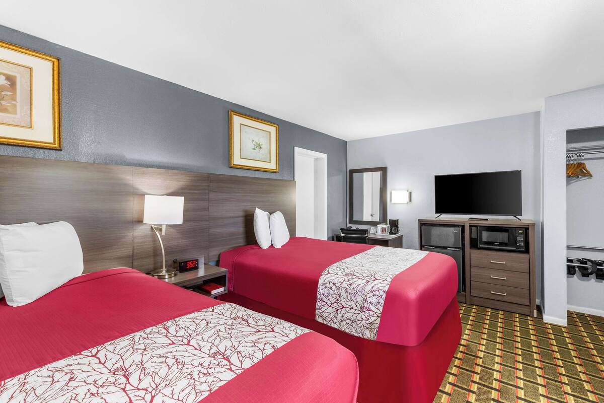 A hotel room with two beds, a TV, a desk with a computer, and a wardrobe.