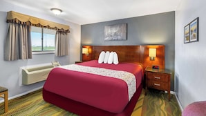 A hotel room with a large bed, a bedside table with a lamp, a wall-mounted air conditioner, and a window with curtains. - Americas Best Value Inn Belleville (Belleville)