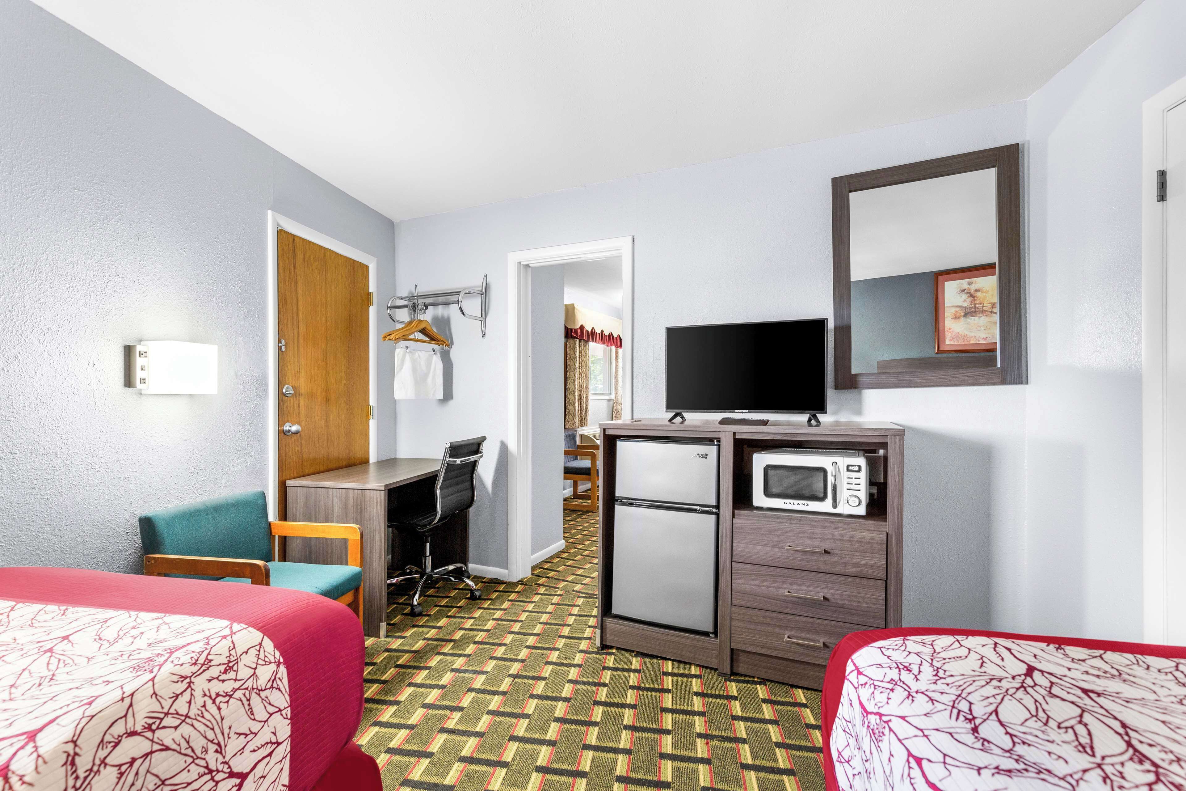 Une chambre d’hôtel avec deux lits, un bureau, une chaise, une télévision, un four à micro-ondes et un réfrigérateur.