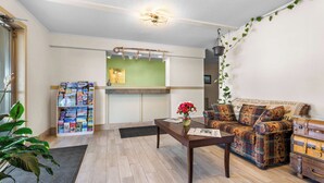 A cozy living room with a wooden coffee table, a patterned sofa, a bookshelf with magazines, and a hanging plant. - Americas Best Value Inn Belleville (Belleville)