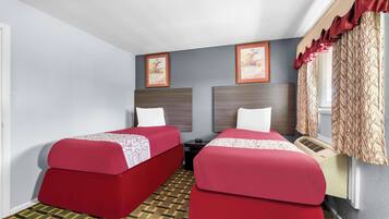 Ein Hotelzimmer mit zwei Einzelbetten, einem kleinen Tisch, einem Heizkörper und einem Fenster mit Vorhängen.