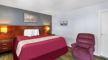 Hotelkamer met een groot bed, houten hoofdeinde, twee bedlampen, een stoel en een deur.