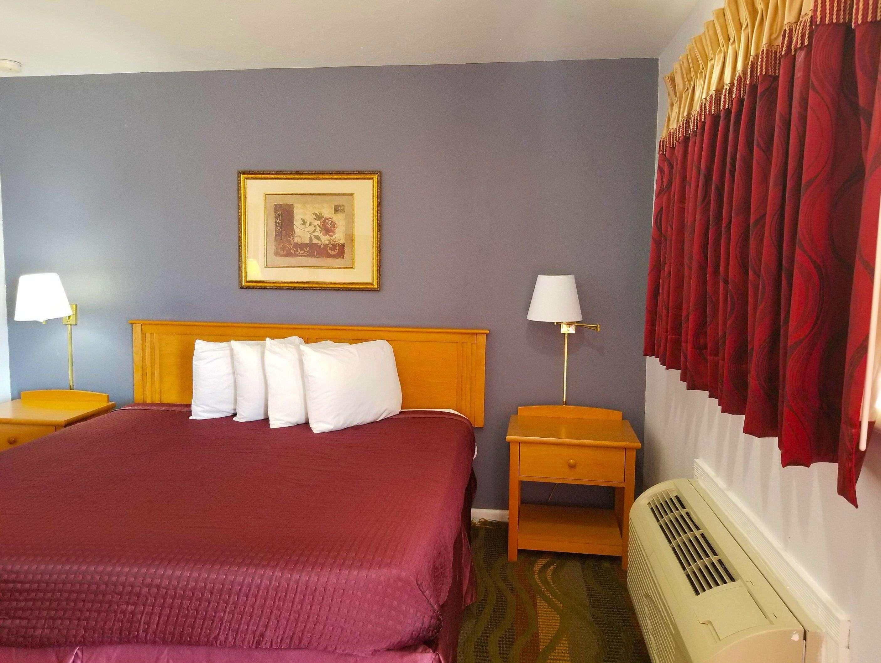 Une chambre d’hôtel avec un lit, deux tables de chevet, un tableau accroché au mur, un radiateur et des rideaux rouges.