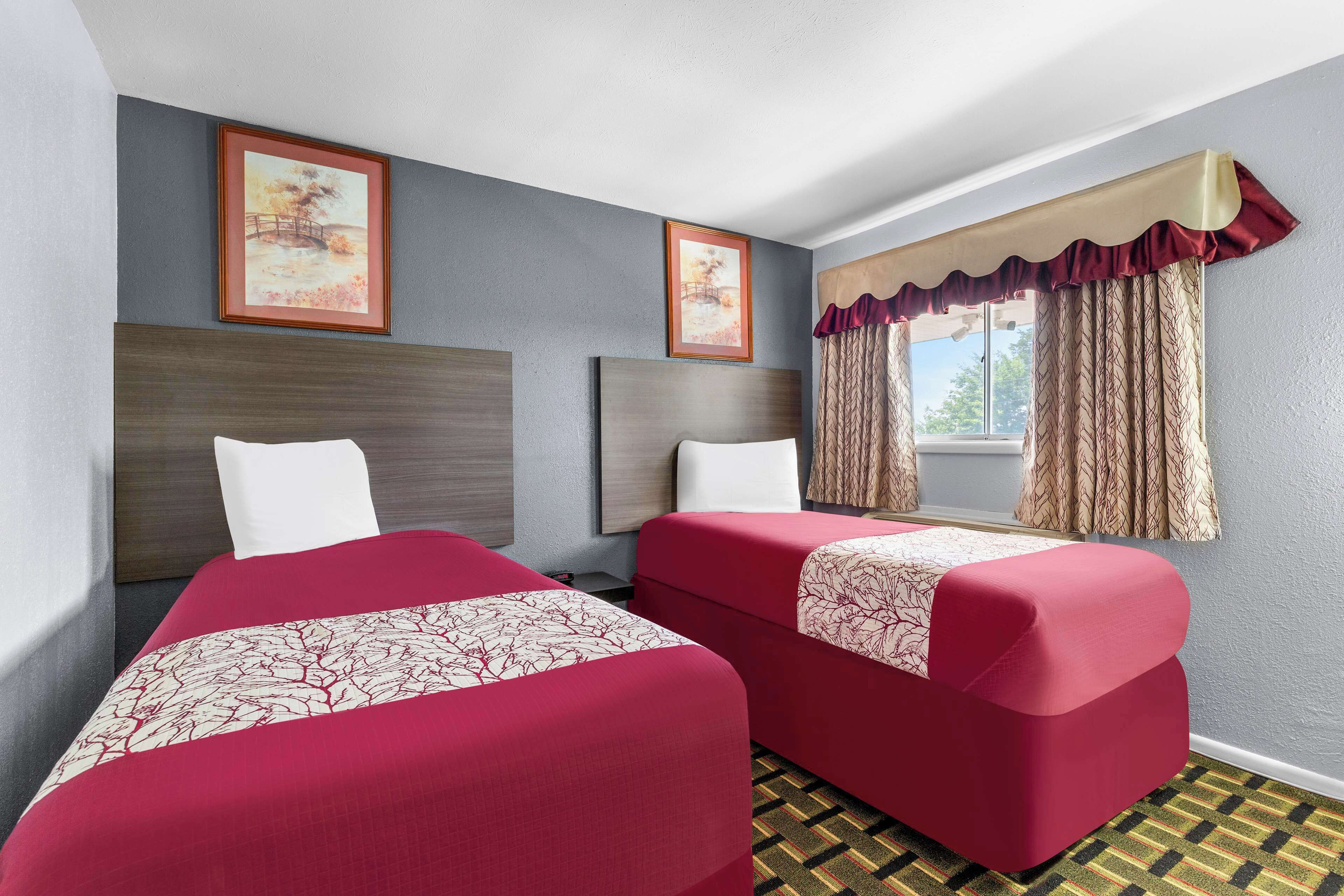 Habitación de hotel con dos camas, un ventanal con cortinas y dos cuadros en la pared.