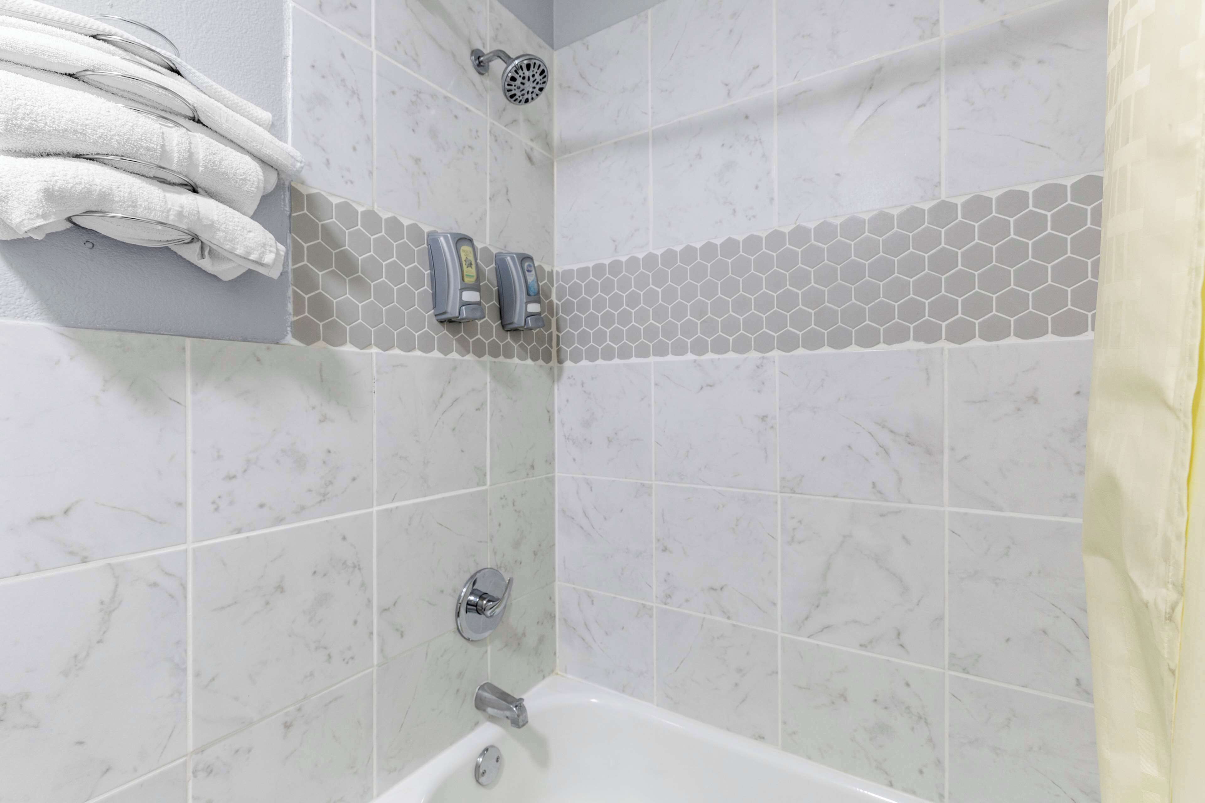 A bathroom with a shower, a towel rack, and a soap dispenser.