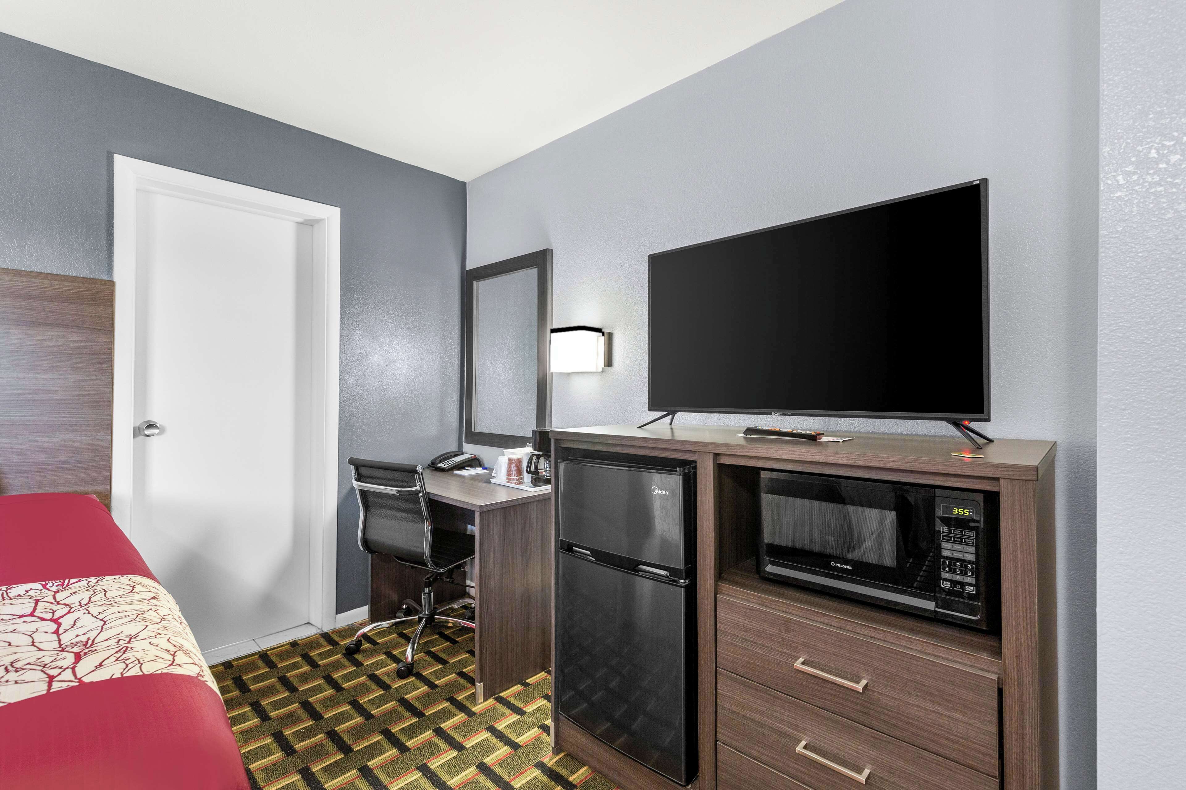 Una habitación de hotel con una cama, un escritorio con computadora, un refrigerador, un microondas y un televisor.