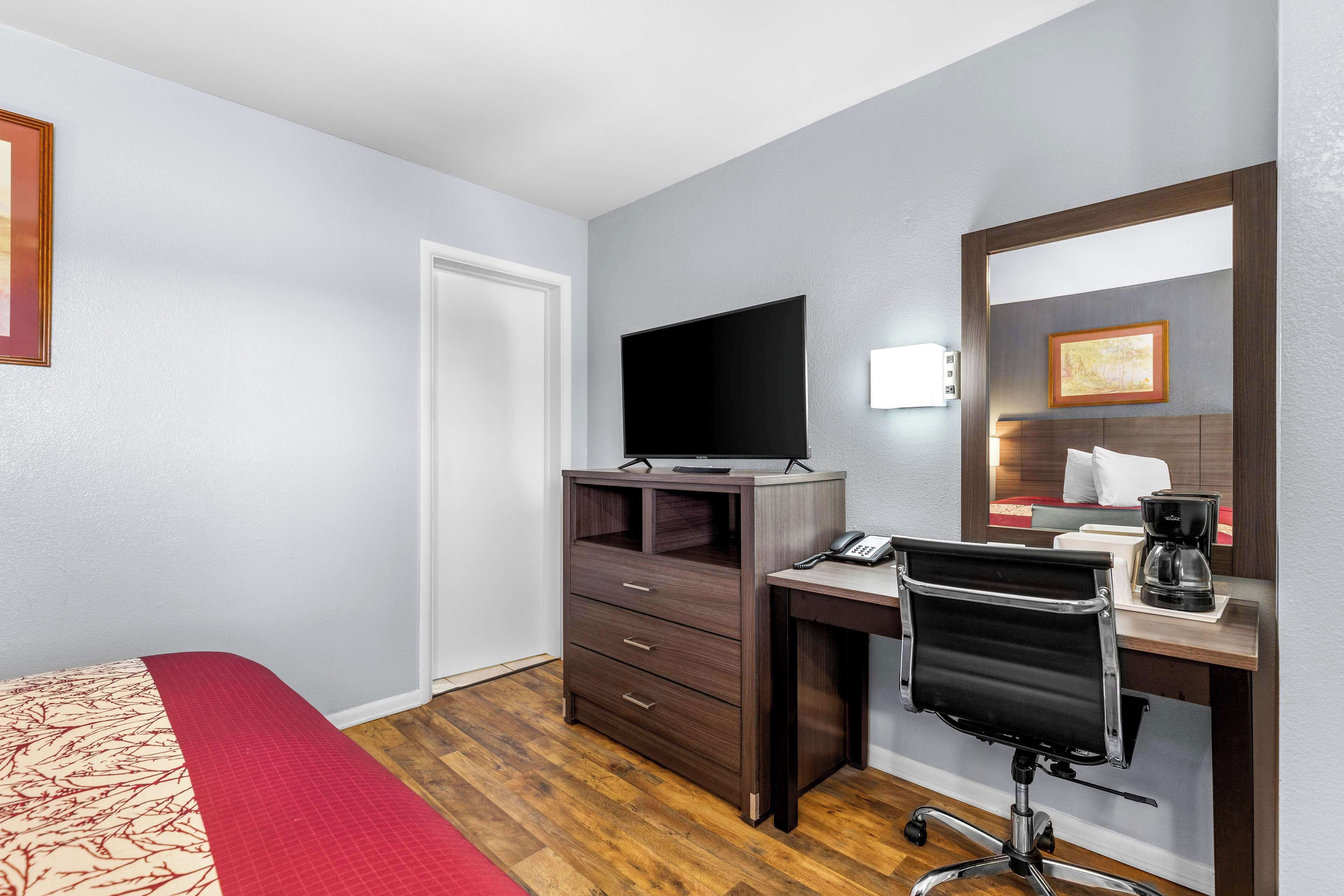 Habitación de hotel con cama, escritorio con silla, televisión de pantalla plana, teléfono y cafetera.