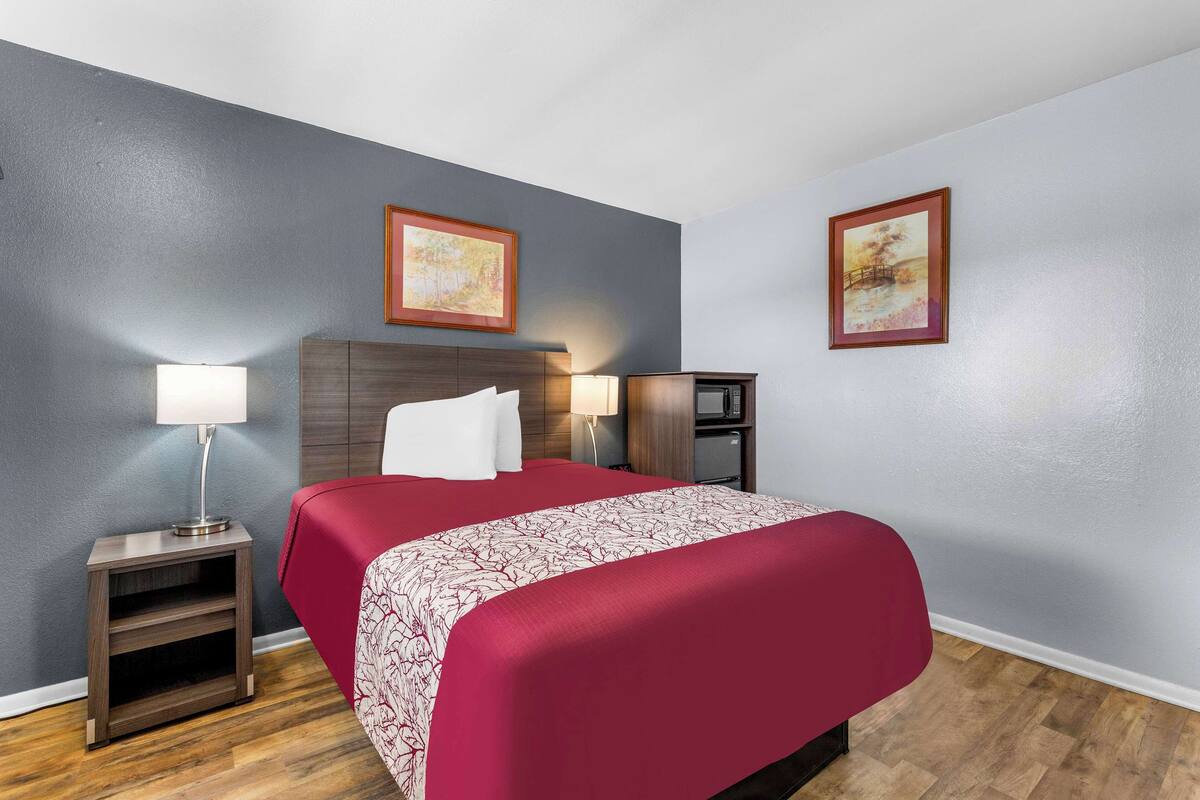 A hotel room with a bed, two bedside tables, a nightstand, a lamp, and two framed pictures on the walls.