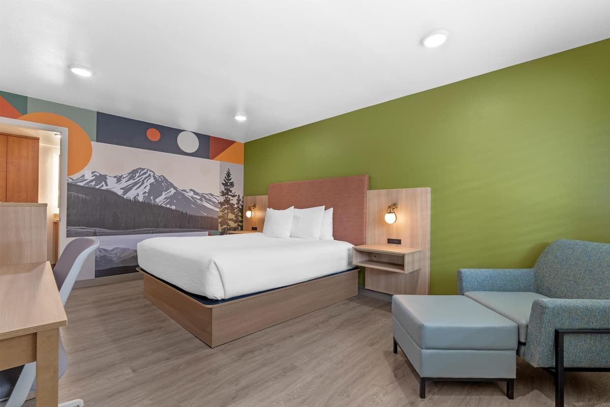 Ett modernt hotellrum med en säng, ett skrivbord, en stol och en väggmålning.
