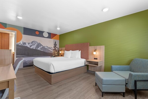 A modern hotel room with a bed, a desk, a chair, and a wall mural.