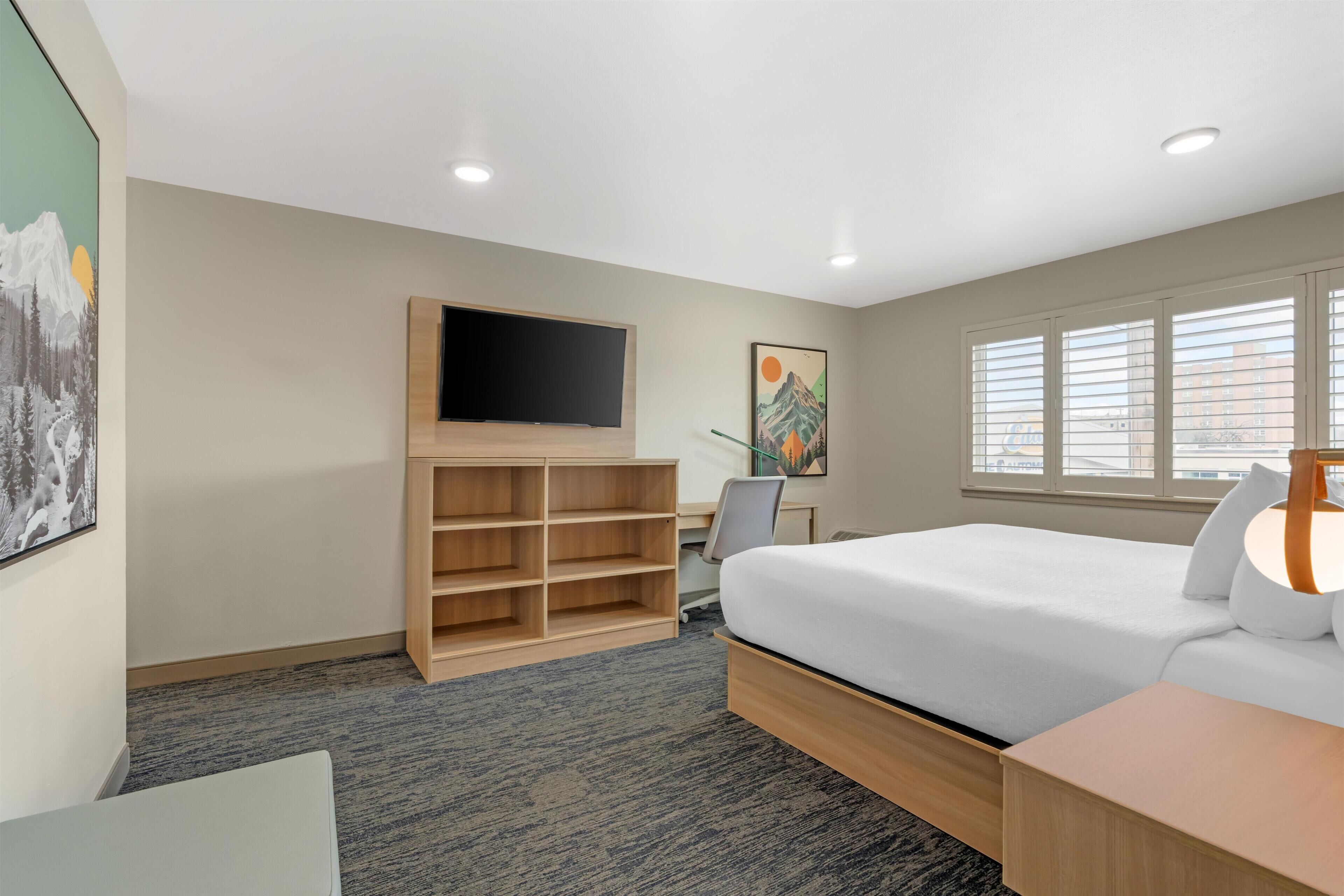 A hotel room with a bed, a TV, a desk, and a chair.