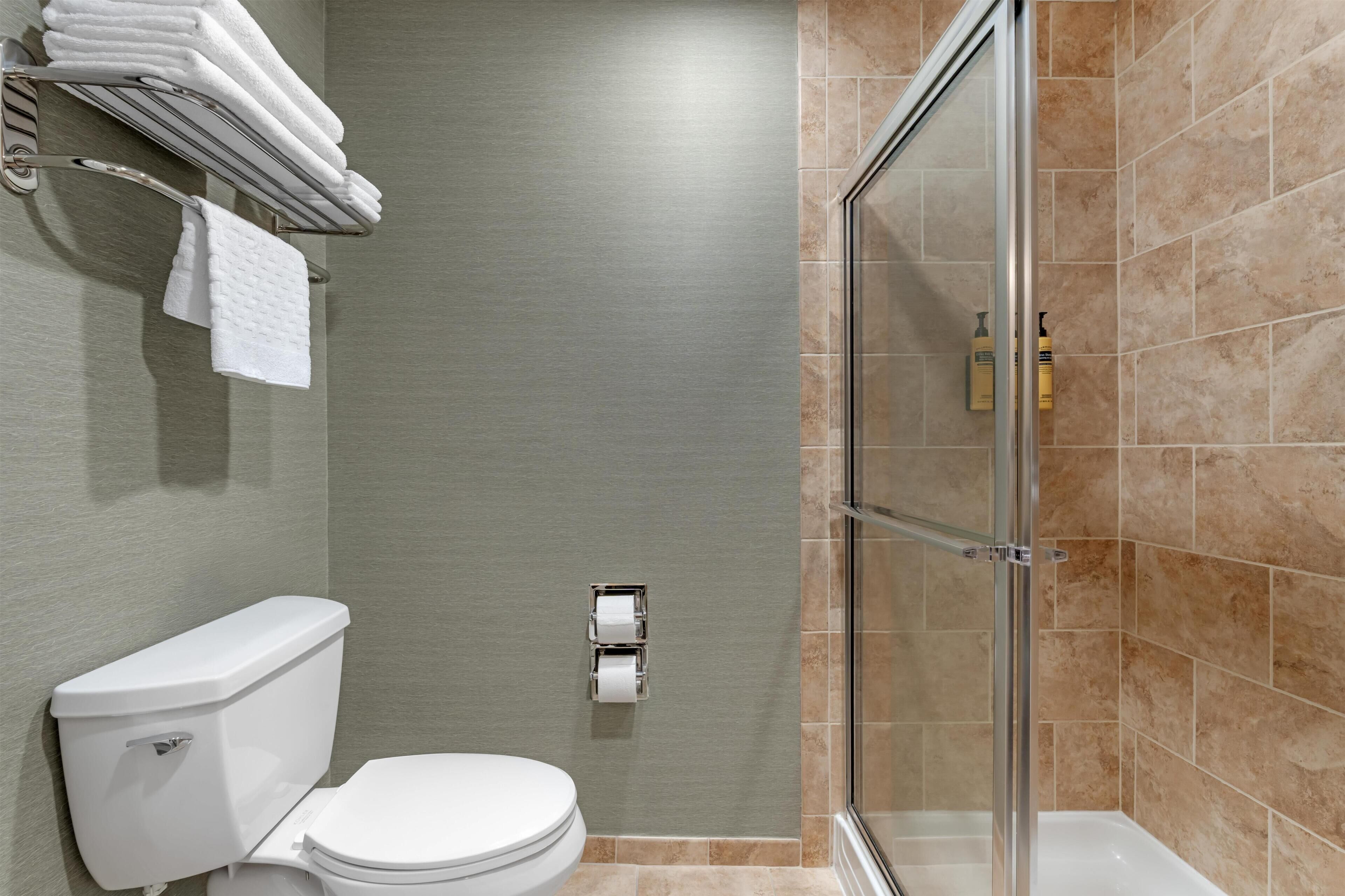 Un baño con inodoro, cabina de ducha de vidrio y toallero con toallas dobladas.